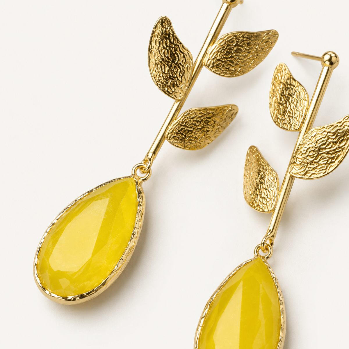 Close view of textured leaf details and the mustard yellow drop accent on gold earrings.