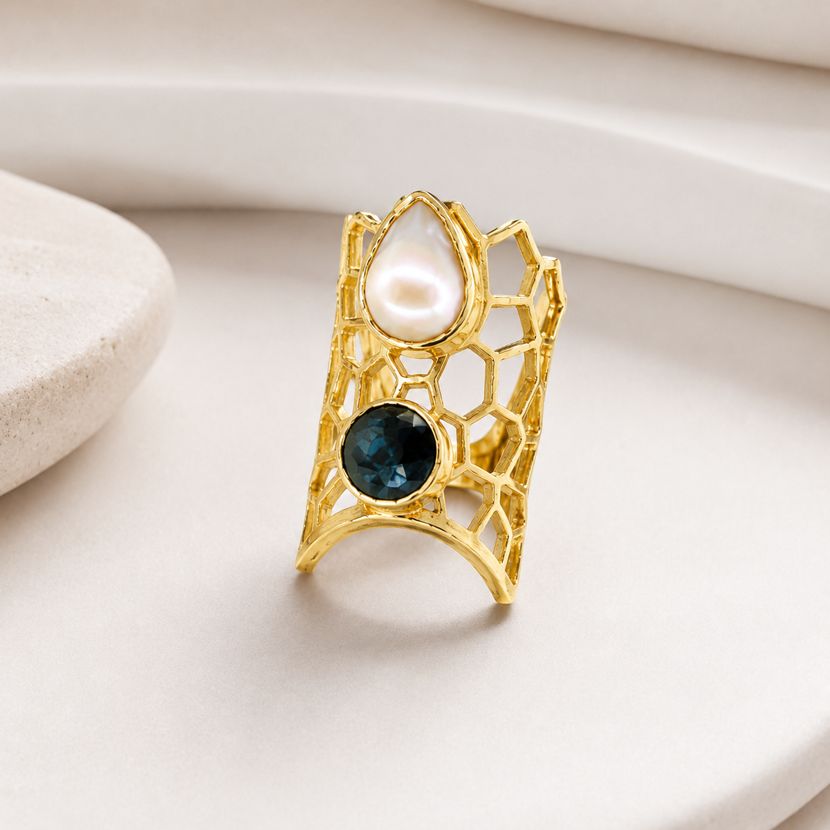 Angled view of a gold-plated statement ring with honeycomb openwork and two round stone accents.