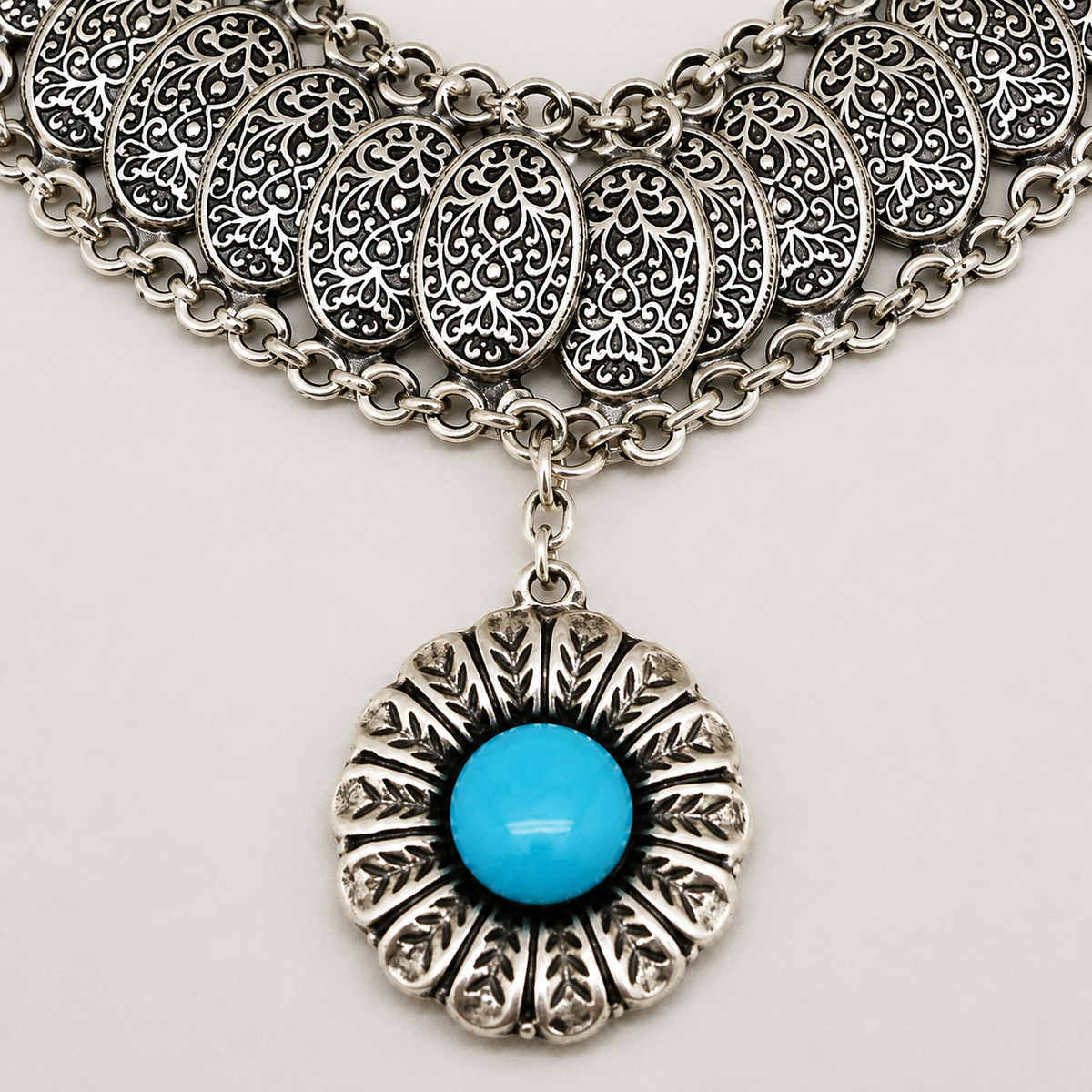 Close view of the necklace’s ornate medallion links and turquoise center.