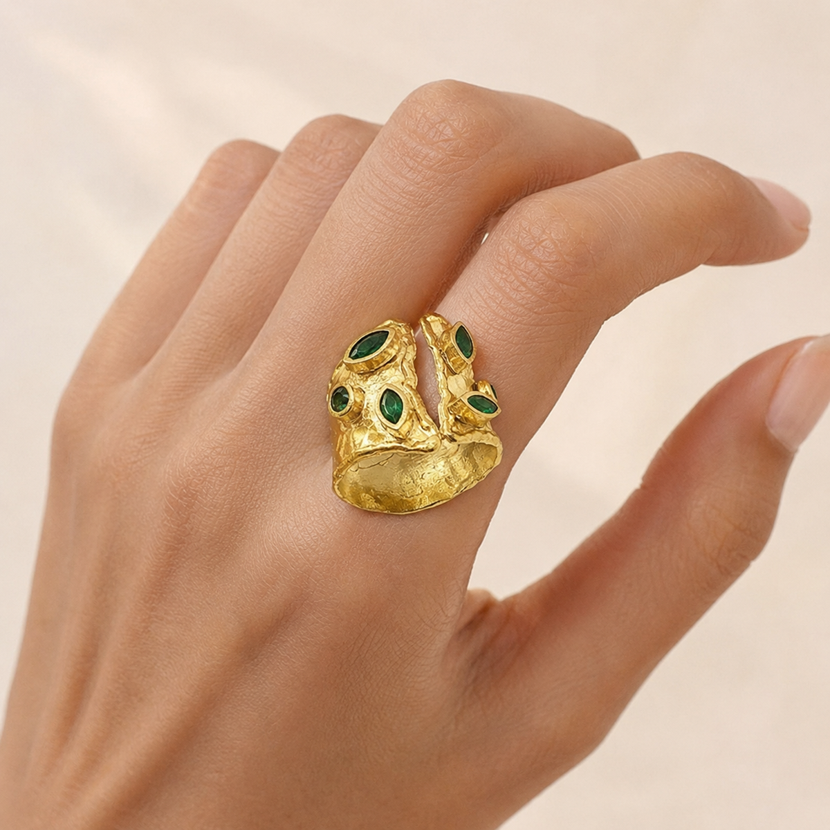 Gold-plated open cuff ring with emerald green stones on a white background