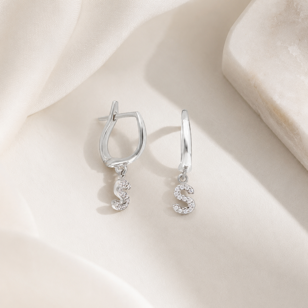 Personalized huggie earrings with a dangling initial charm in a silver-tone finish.