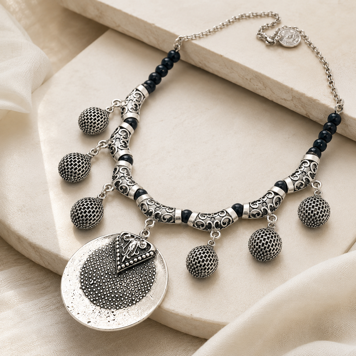 Angled view of a black bead necklace with a silver-toned medallion pendant.