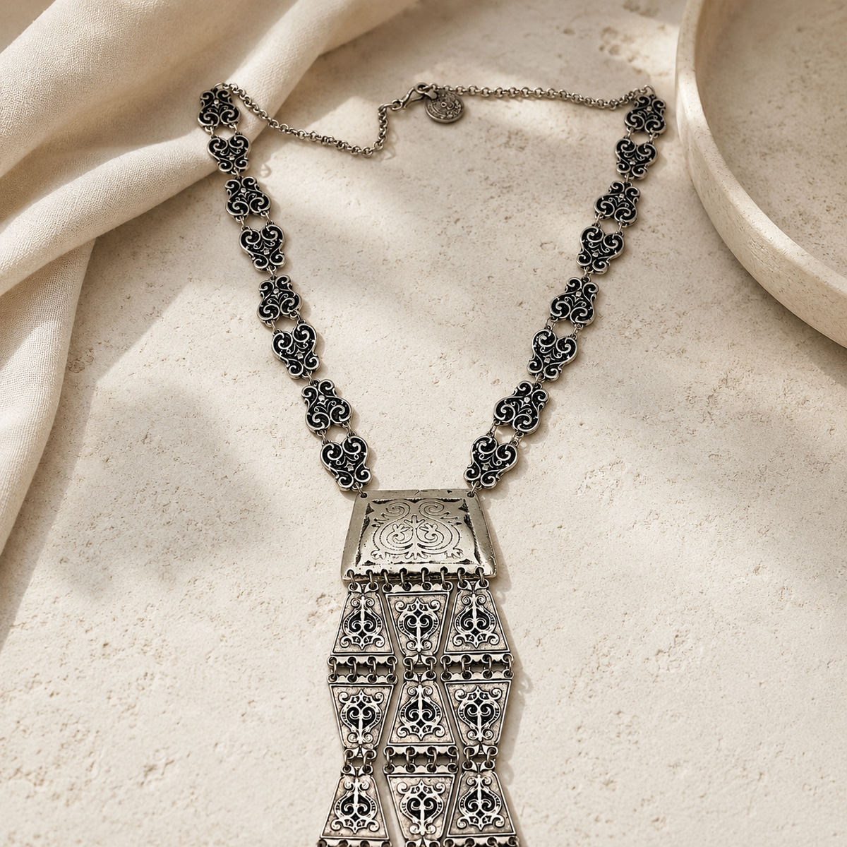 Silver-tone statement necklace with ornate triangle links and tassel pendant.