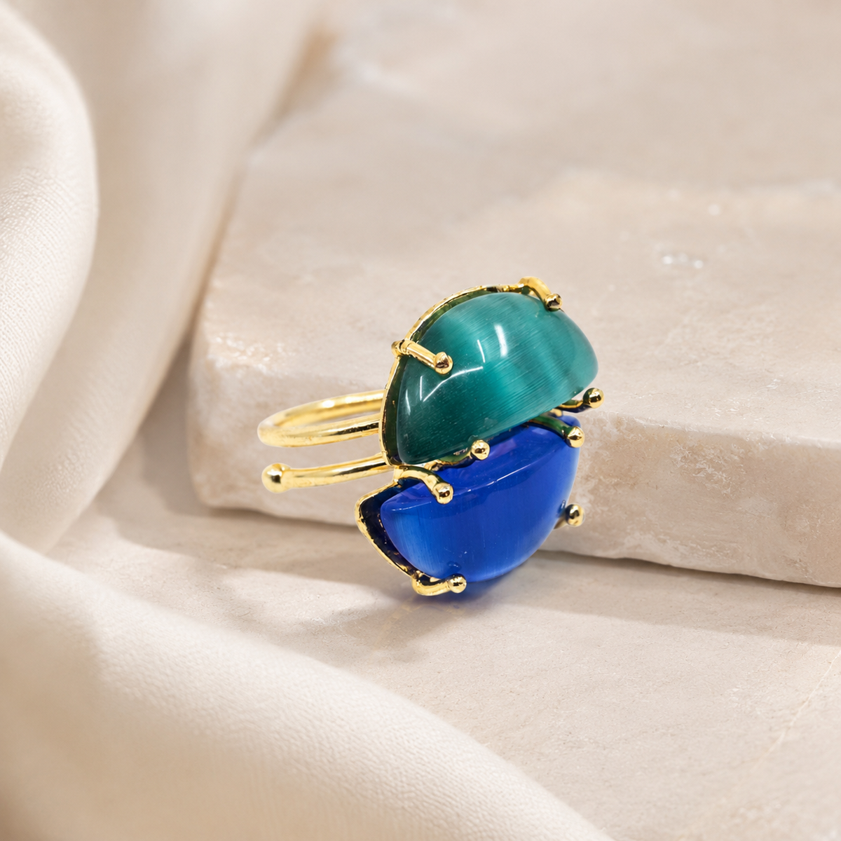 Gold-plated adjustable ring with two cat-eye style stones in blue and teal on a white background.