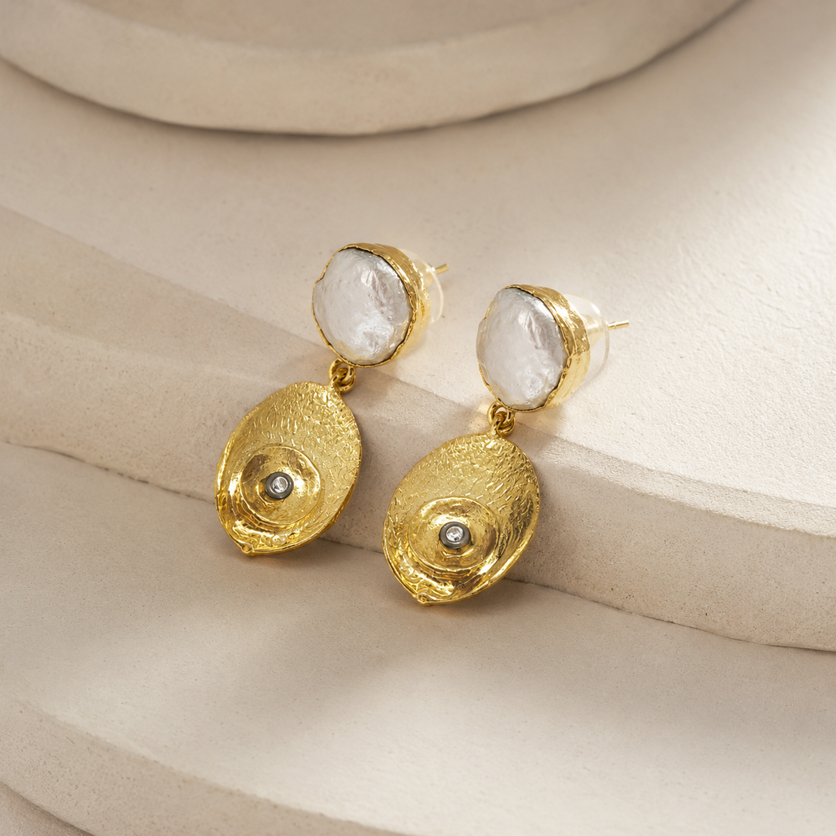 Side angle of pearl-like oval drop earrings with hammered gold-plated detail.