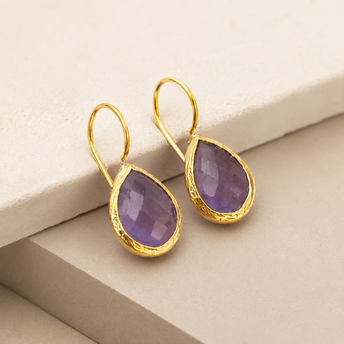 Angled view of teardrop amethyst earrings with gold-plated hooks.