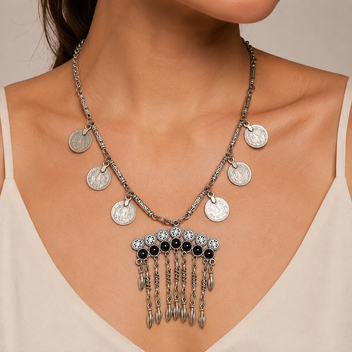 Silver-tone necklace with layered coin details and black stone accents on a white background.
