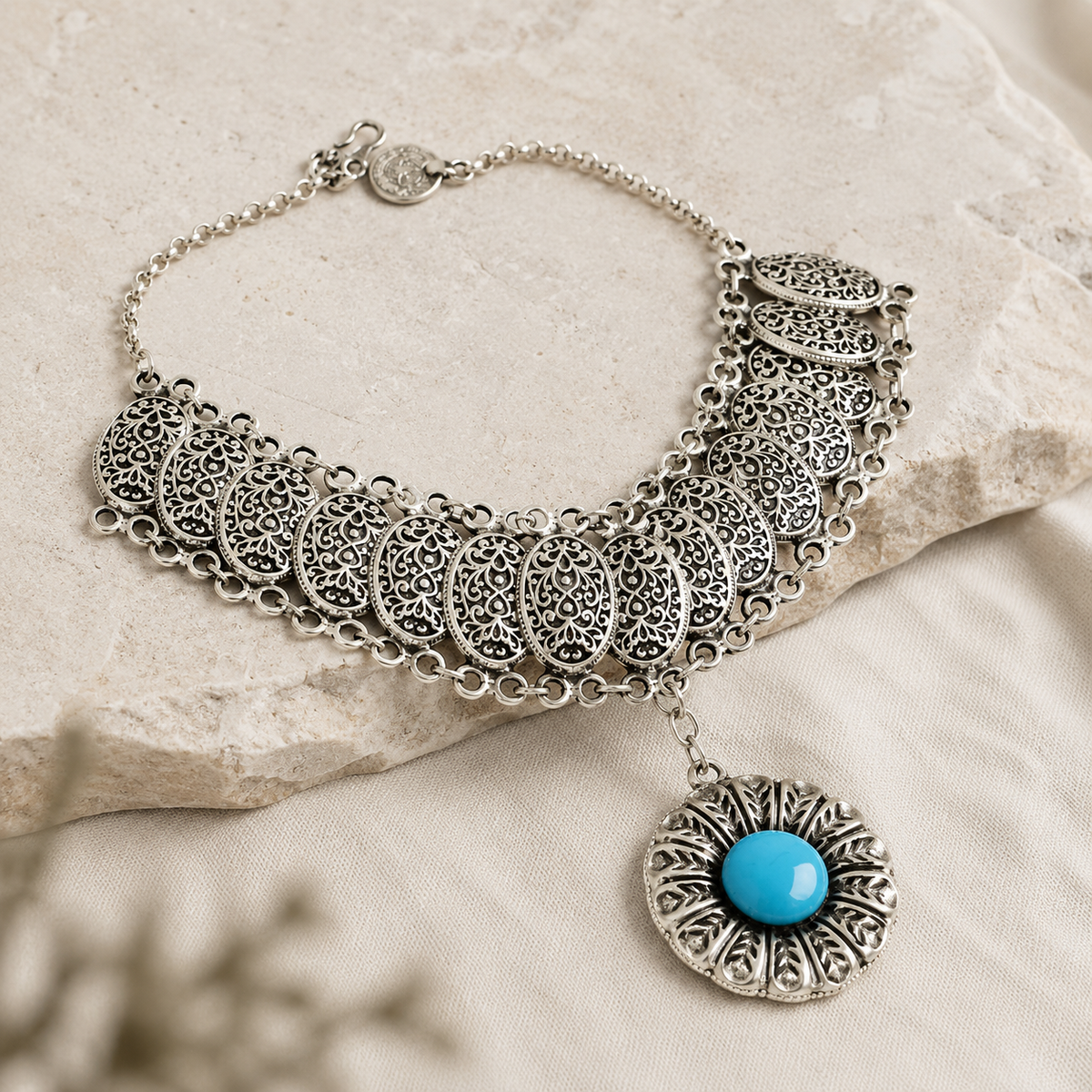 Angled view of a silver-tone filigree medallion necklace with turquoise center.