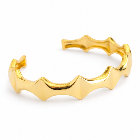 An angled view of a polished gold-tone open cuff bracelet.