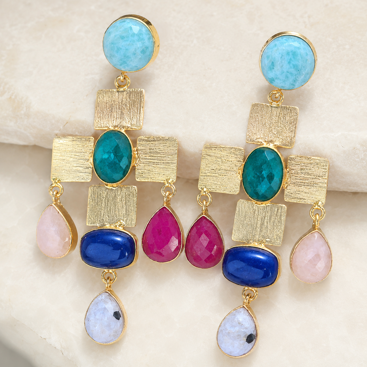 Close-up of gold-plated statement earrings with textured square links and colorful stone accents.