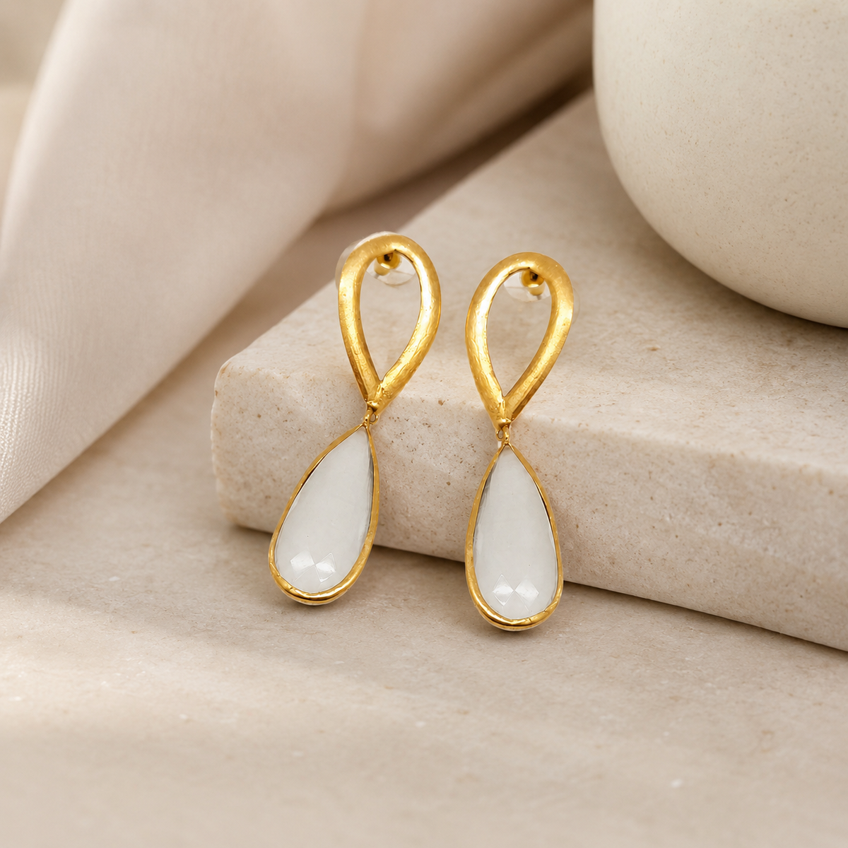 Gold-plated modern drop earrings with a hammered oval top and clear drop.
