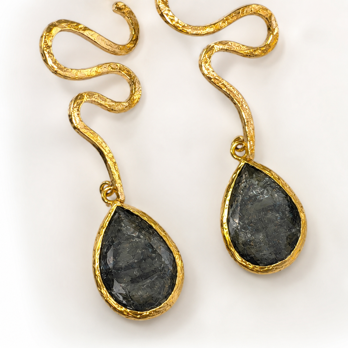 Close view of snake-inspired gold-plated earrings with textured teardrop accents.