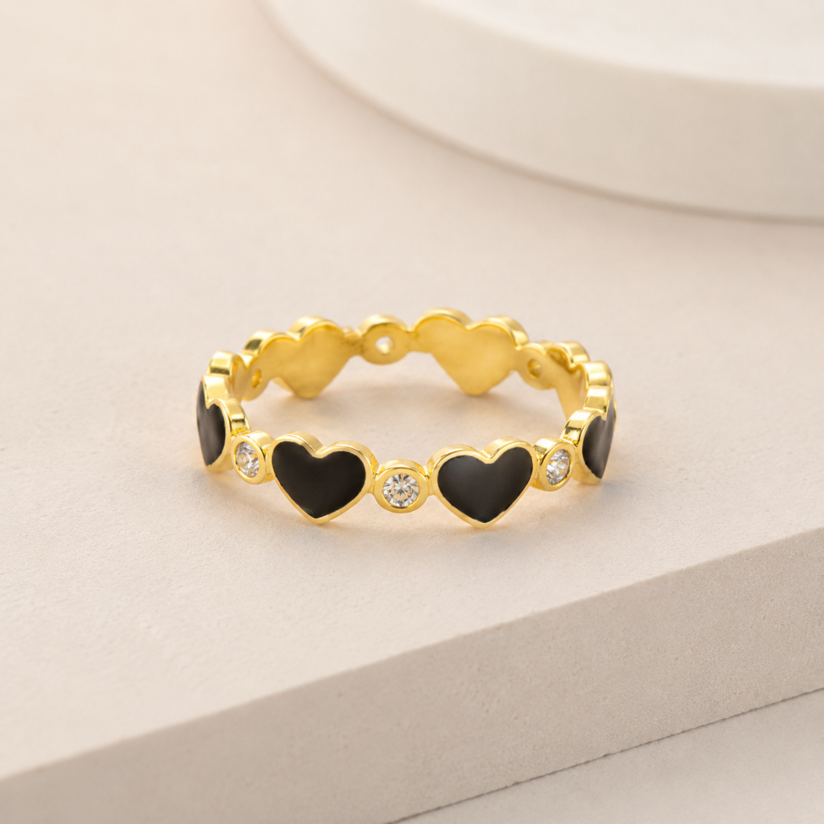 Angled view of a gold-tone ring with black heart shapes and CZ accents.