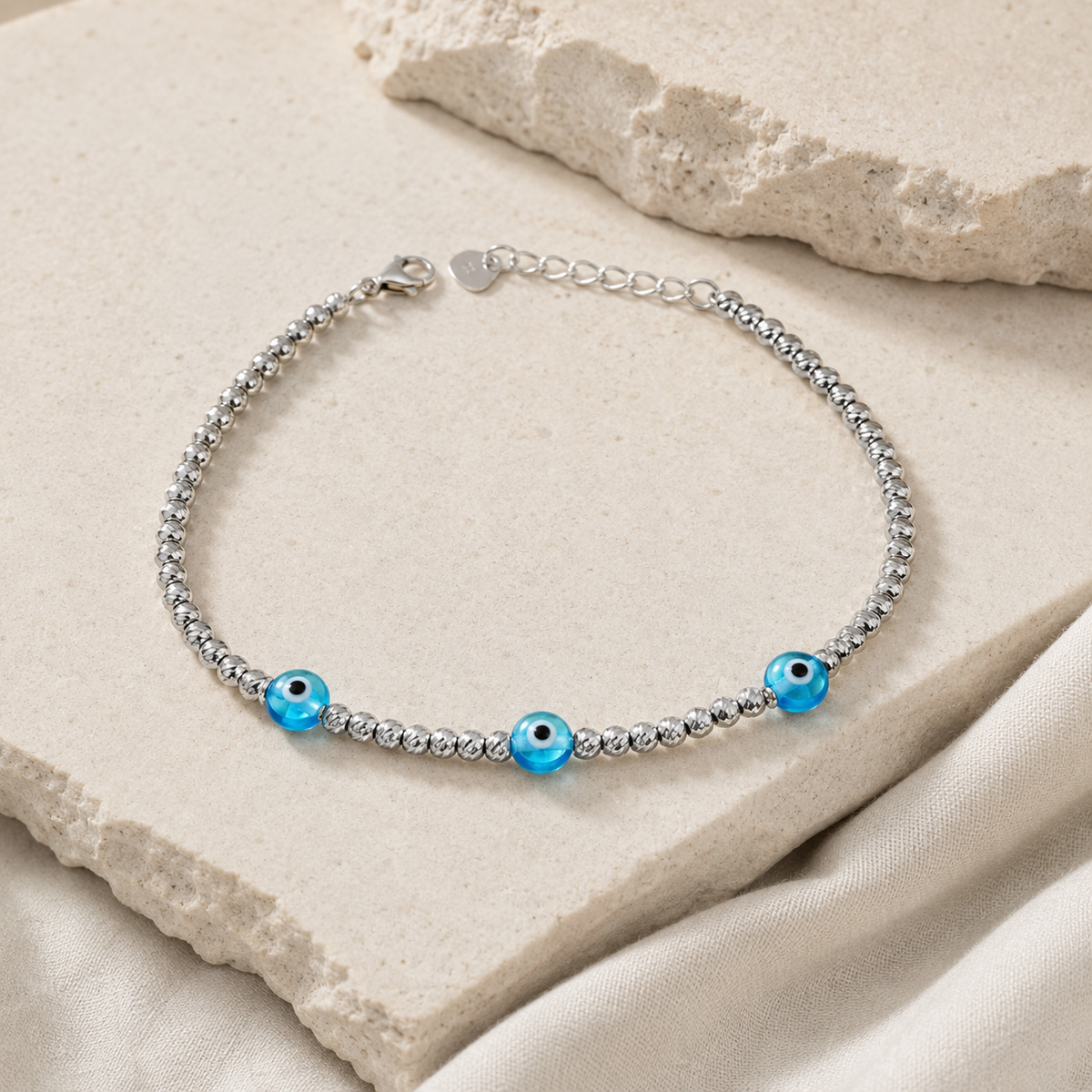 Angled view of a silver bracelet with three blue evil eye accents.