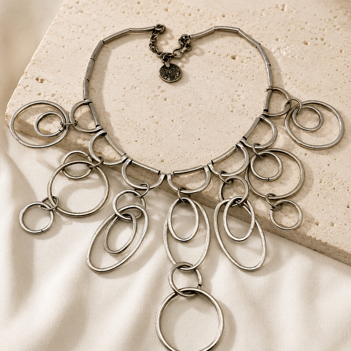 Silver-tone statement necklace with layered ring drops and a sculptural silhouette.