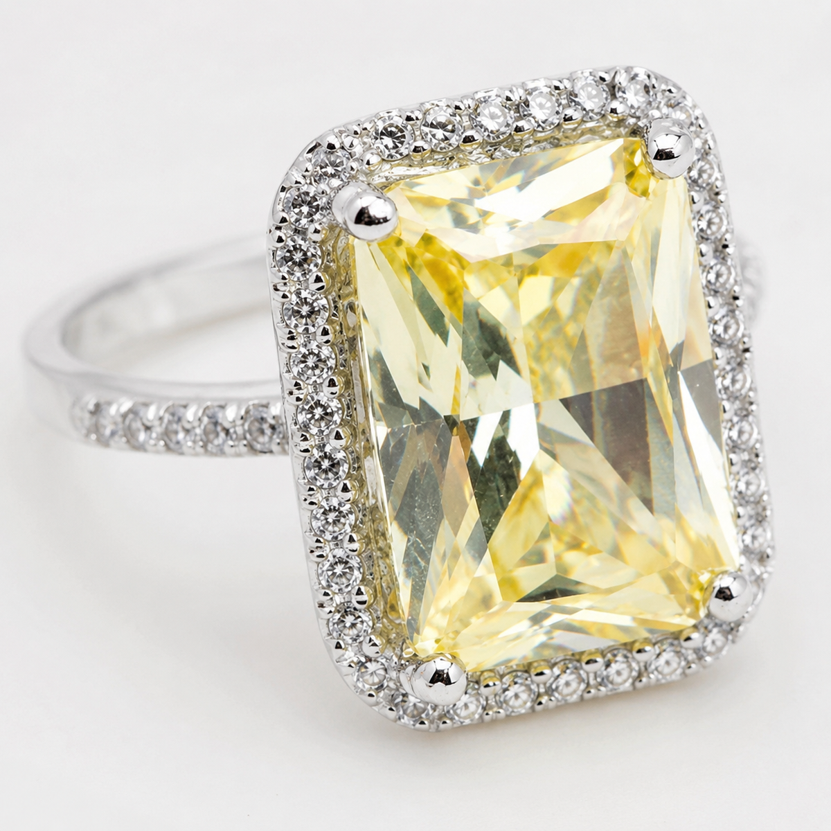 The ring shows a faceted canary center stone framed by a sparkling silver-tone border.