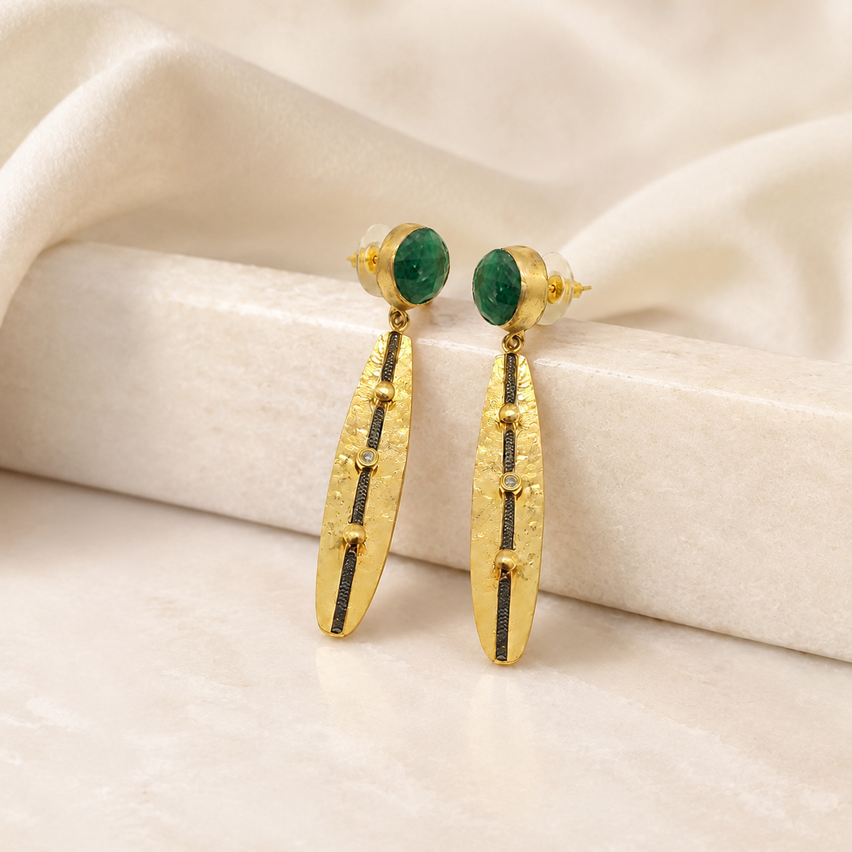 Long gold-plated earrings with green stone accents on a white background.