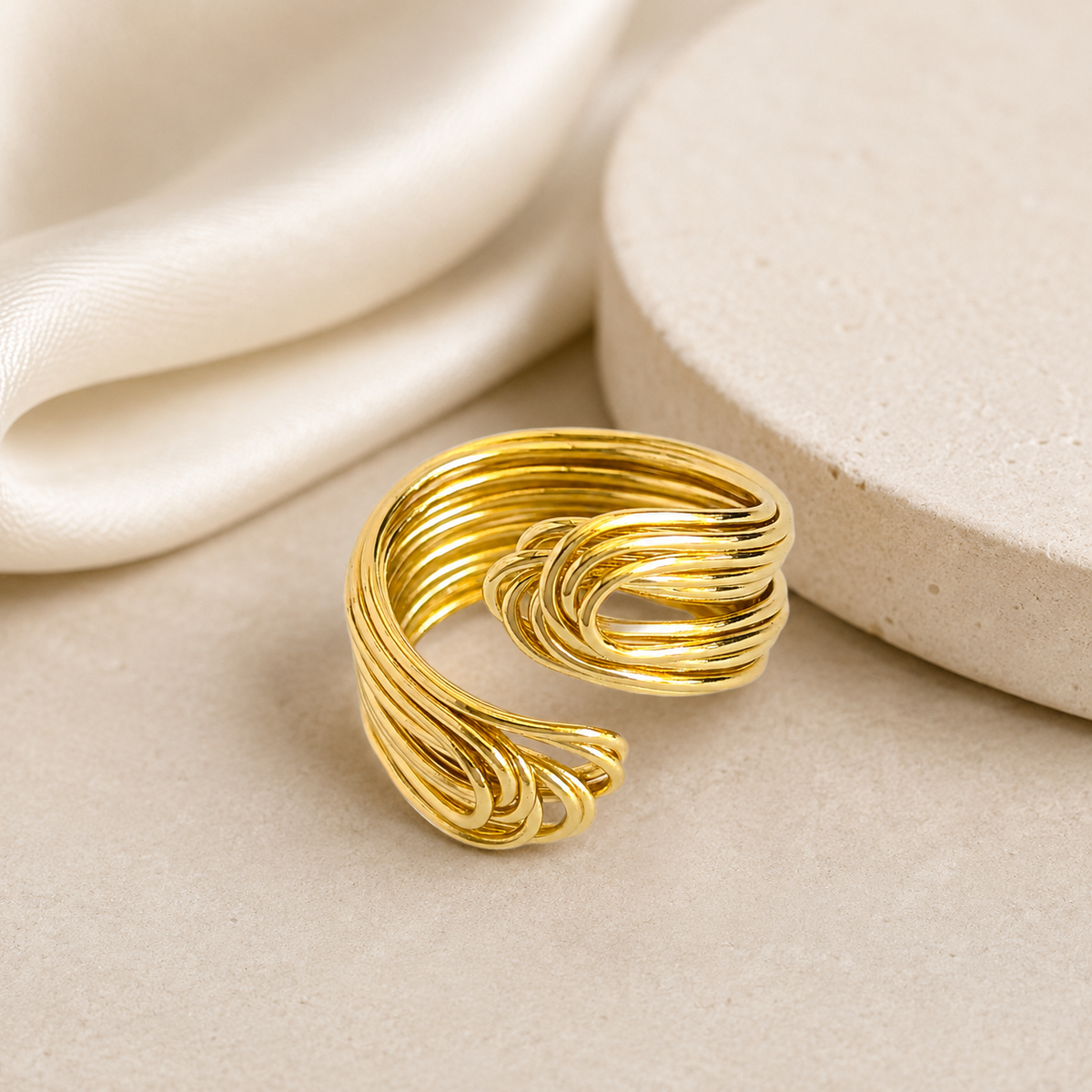 Gold-plated statement ring with a sculptural knot shape on a white background.