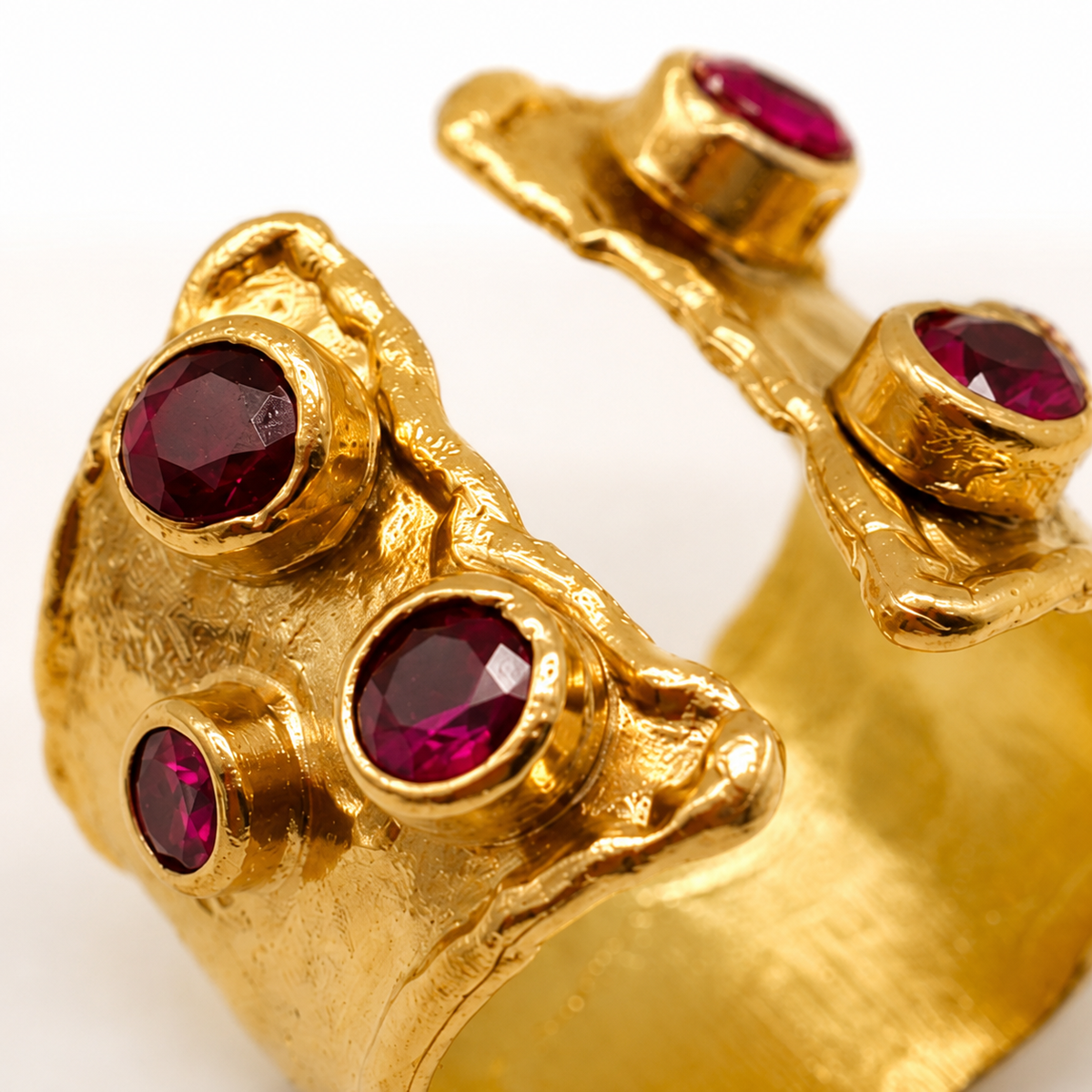 Close-up of a gold-plated ring with ruby pink stones and a textured finish.