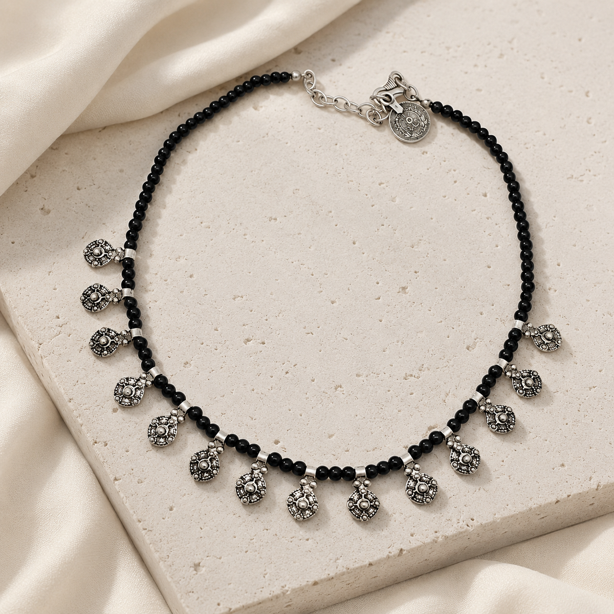 Black bead necklace styled with oval charm drops for a bold look.