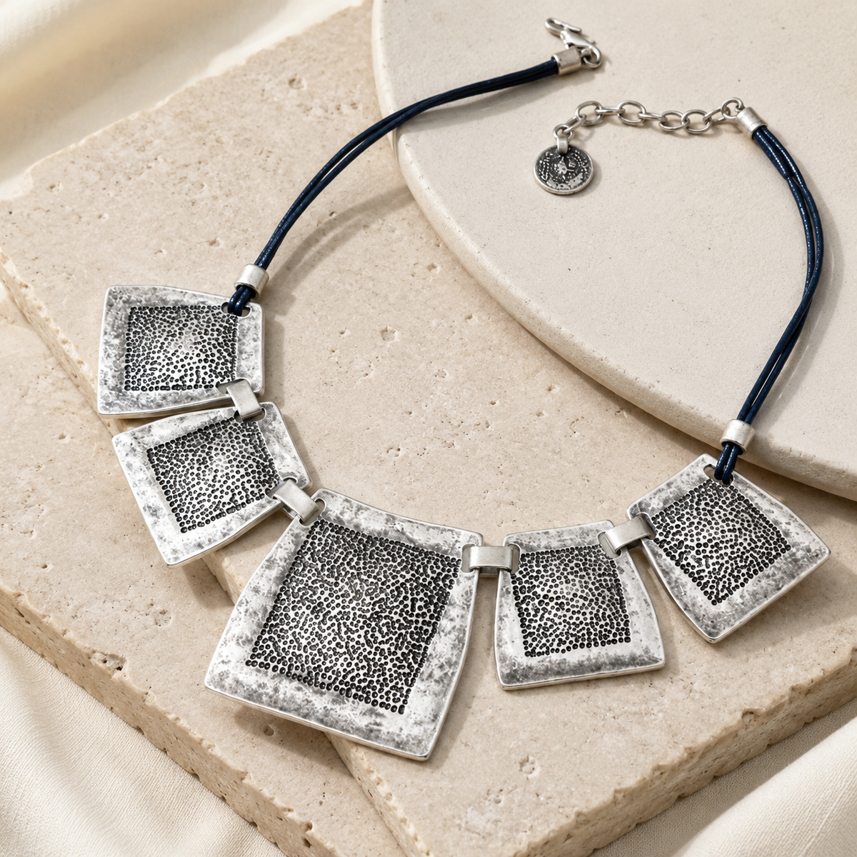 Angled view of the necklace showing the textured square plates and clasp detail.