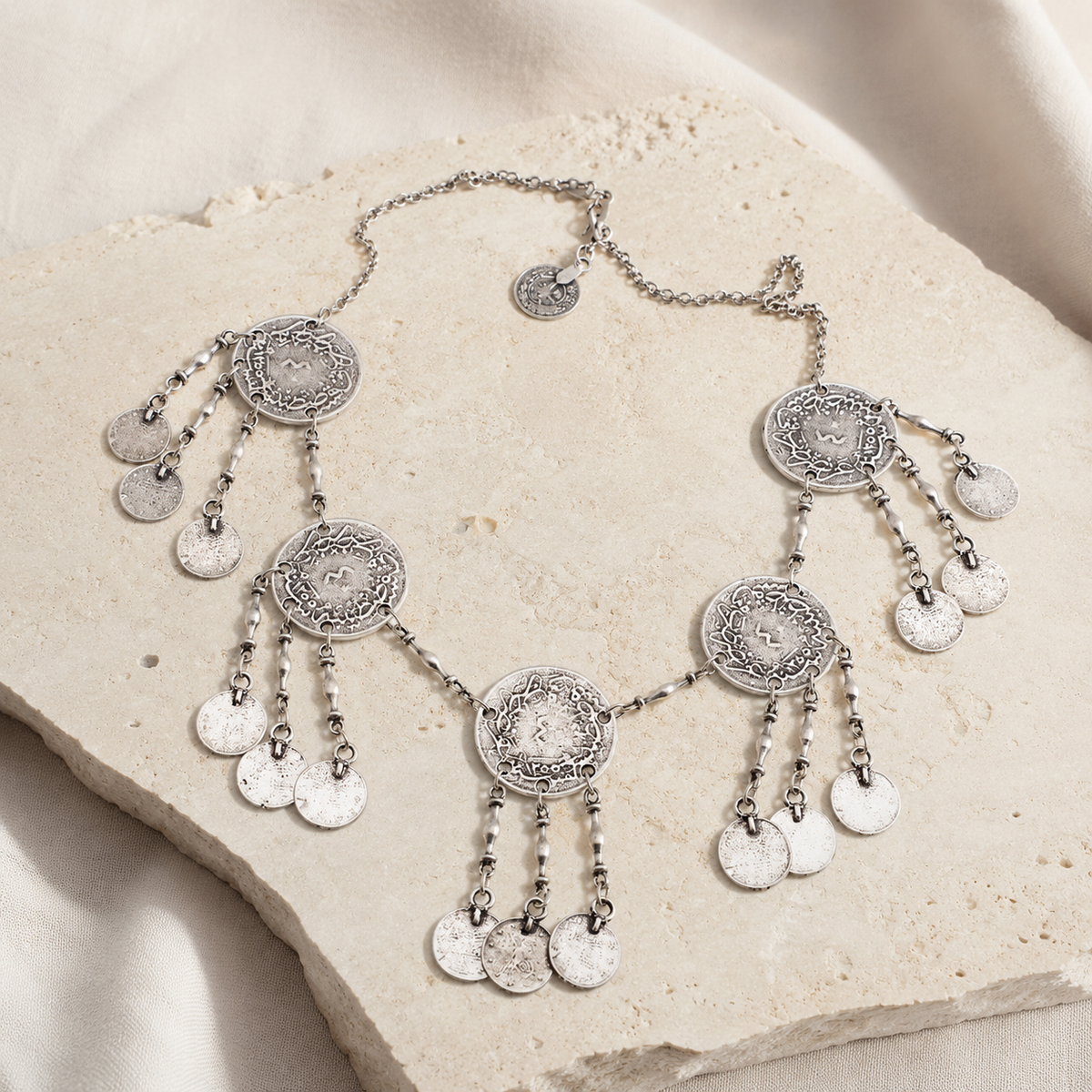 Silver-tone necklace with multiple round coin charms arranged on a white background.