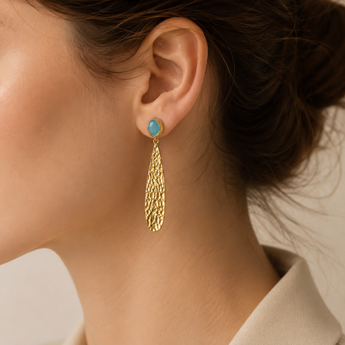 Hammered gold-plated drop earrings with textured long pendants and soft blue oval accents.