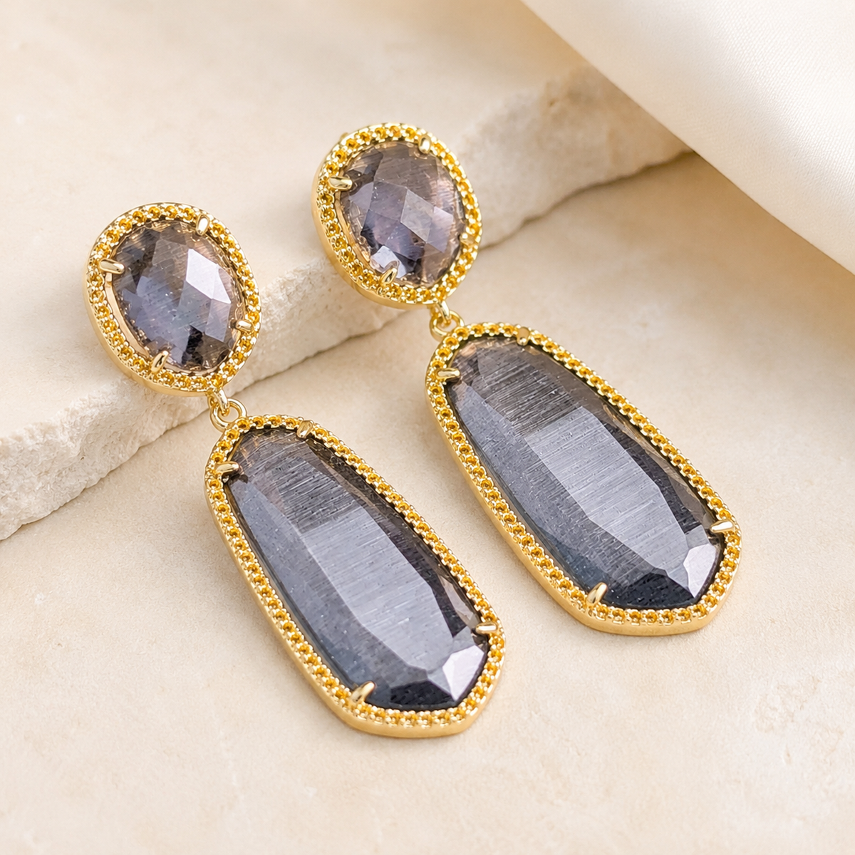 Front view of smoky gray cat eye drop earrings with a gold-plated finish.