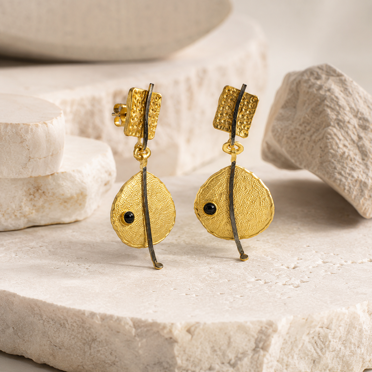 Angle view of textured gold-plated drop earrings with a black bead detail.