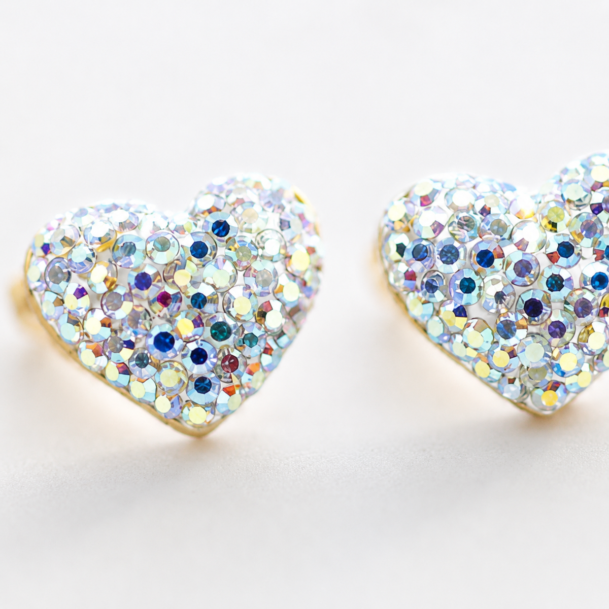 Close view of heart stud earrings with crystal-like detailing and a gold-tone outline.