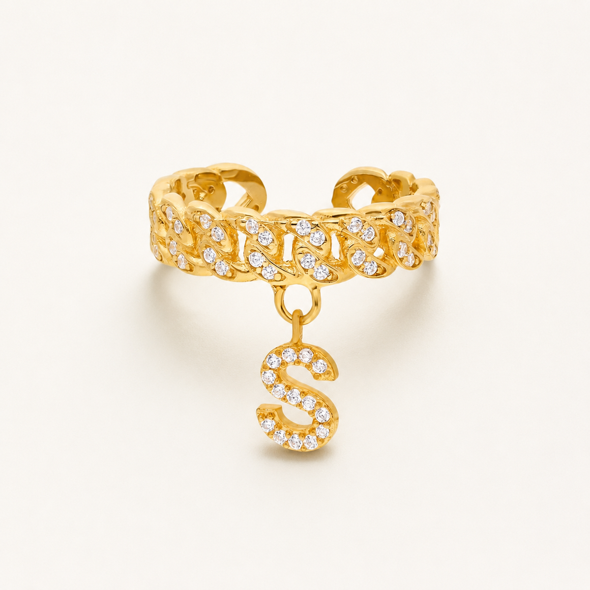 Gold-tone cuff ring with a dangling CZ initial charm and textured linked design.