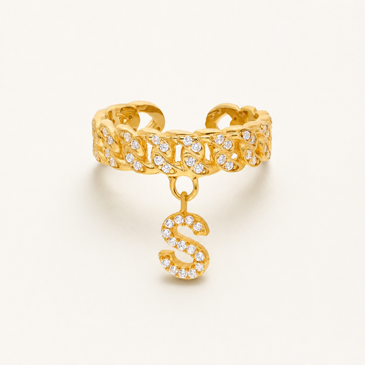 Gold-tone cuff ring with a dangling CZ initial charm and textured linked design.