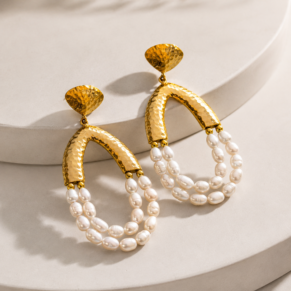 Angle view of gold-tone chandelier earrings with textured arches and pearl drops.