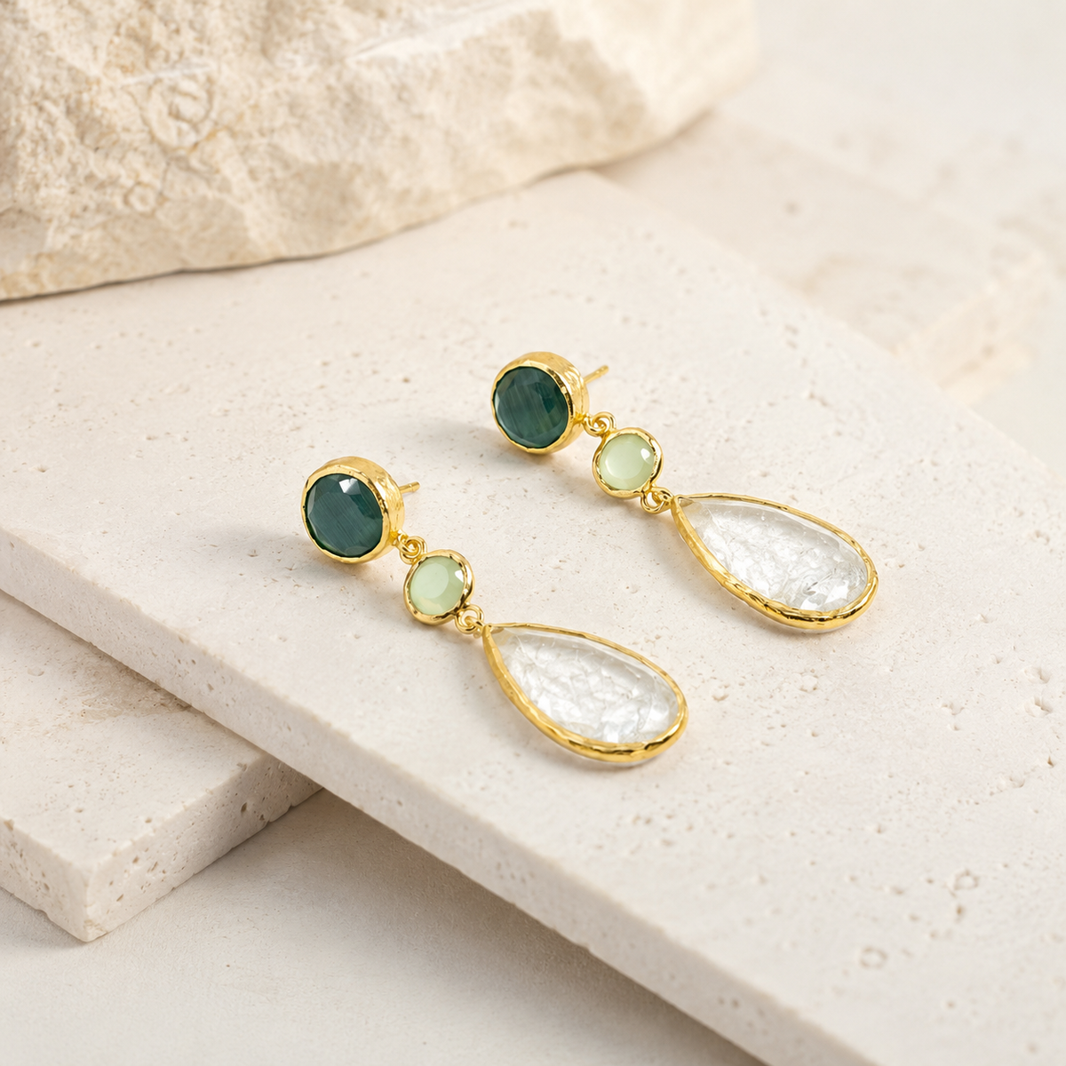 Angle view of gold-plated drop earrings with a teardrop clear stone.
