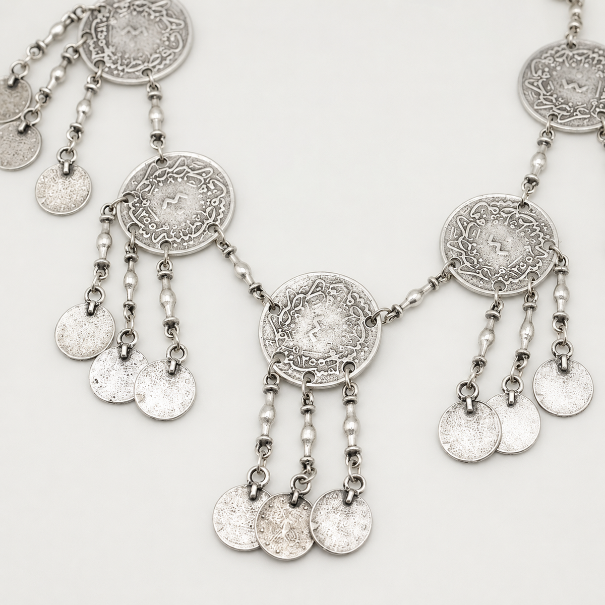 Close view of the textured coin pendant and dangling fringe details.