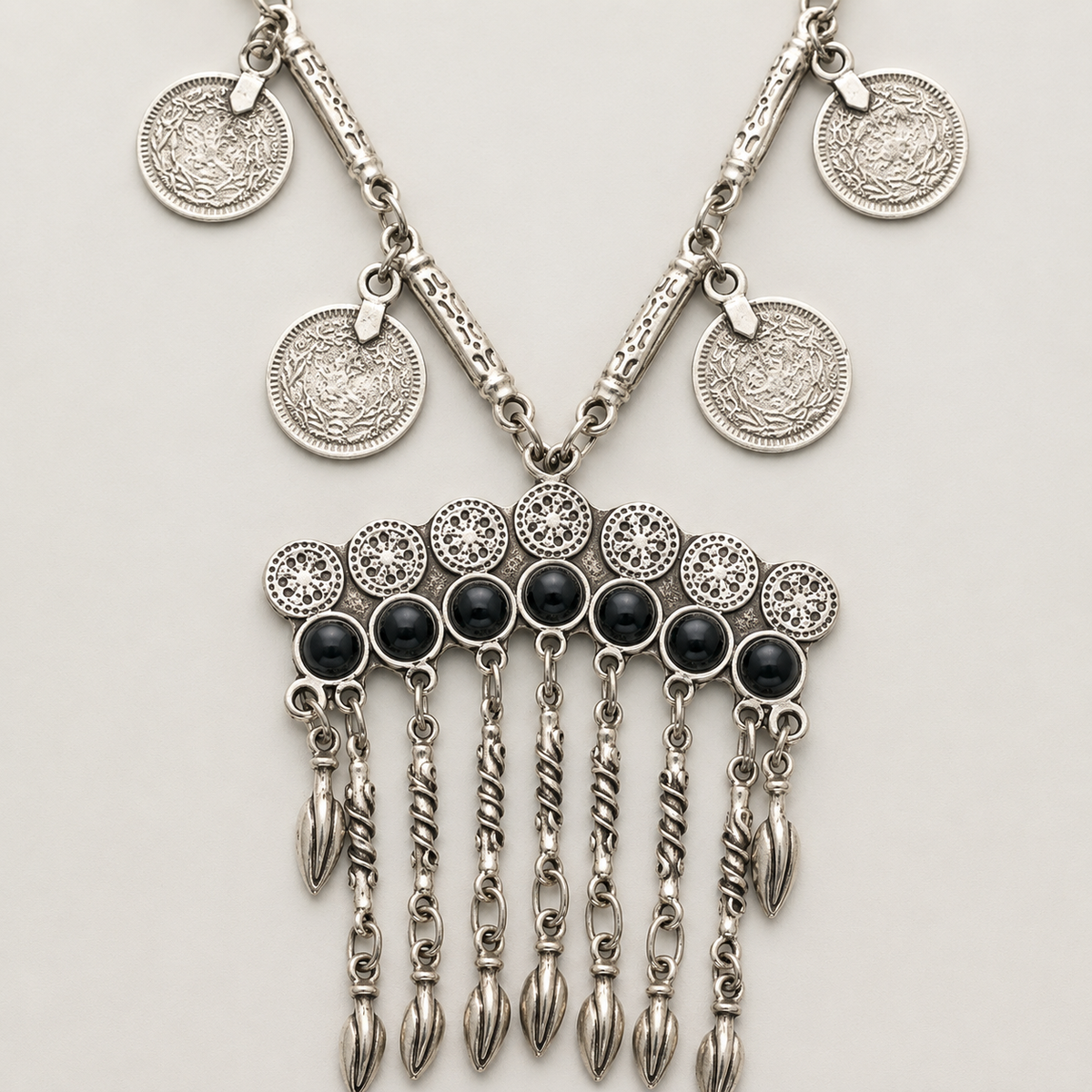 Close view of the silver-tone coin and fringe pendant with black stone accents.