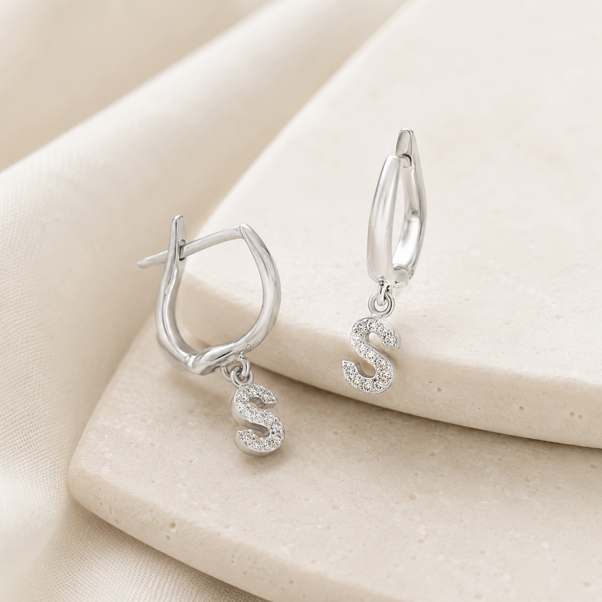 Angle view of silver-tone huggie earrings with a CZ initial pendant.