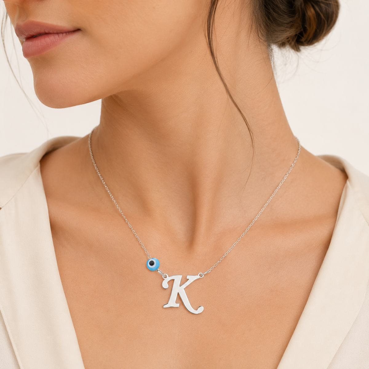 Silver-tone initial necklace with a blue evil eye detail on a slim chain.