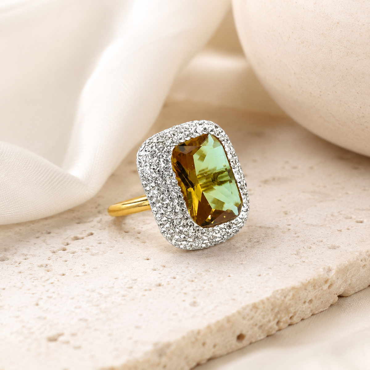 Rectangular faceted center stone ring with a sparkling halo and gold-tone band.