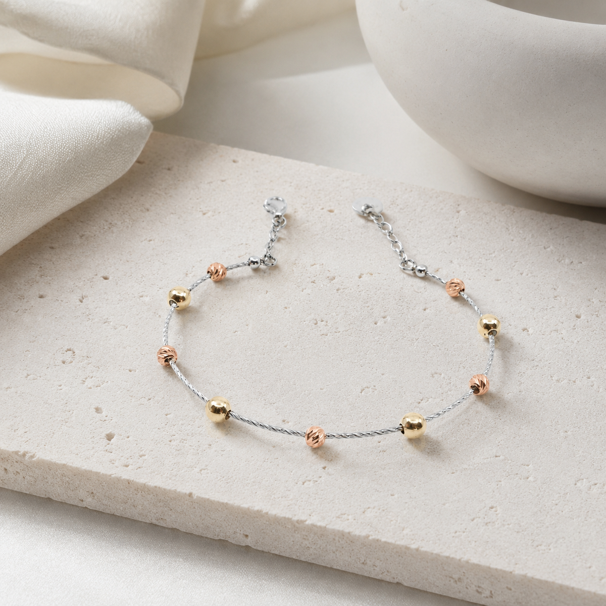 Angled view of a silver bracelet with spaced gold bead accents.