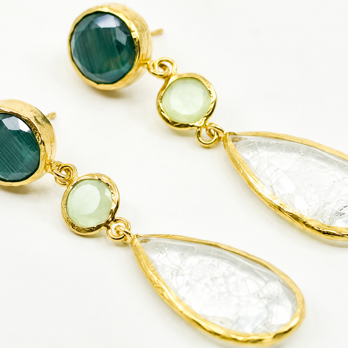 Close view of gold-plated earrings with faceted green and clear stones.