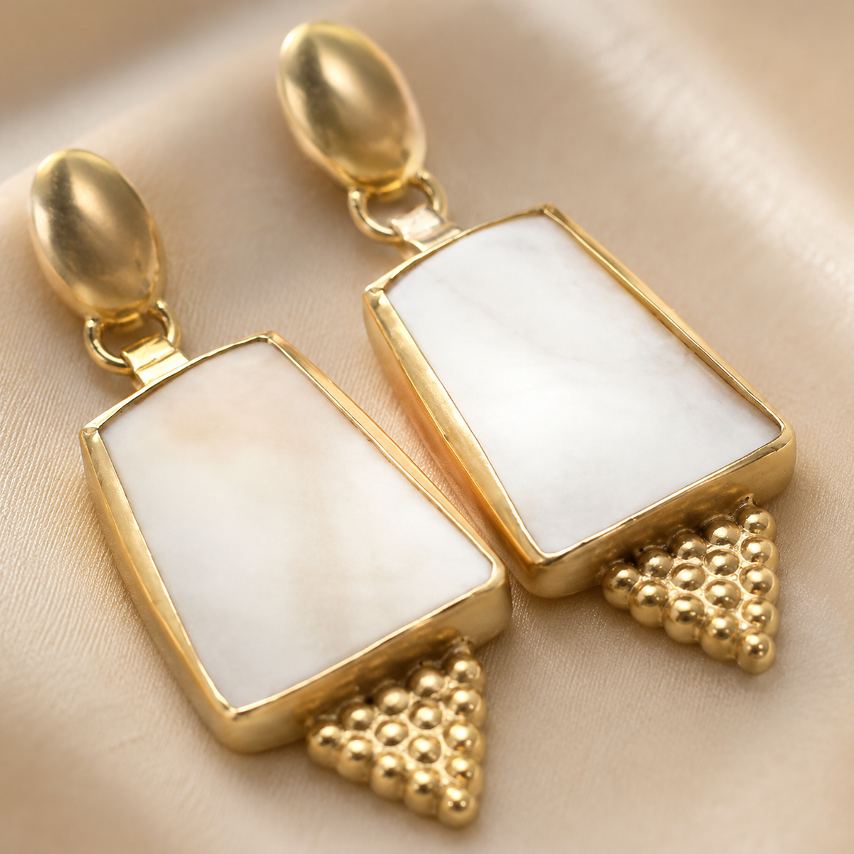 Close view of gold-plated earrings with pearl-like inlays and textured bead-like accents.
