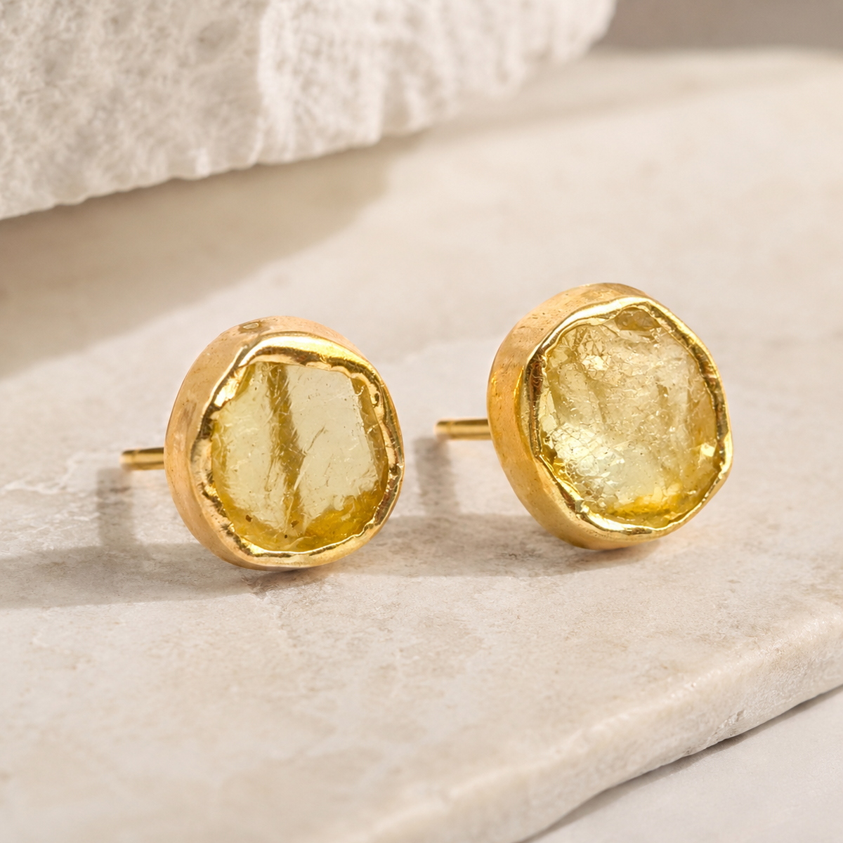 Angle view of rough citrine stud earrings with a textured gold finish.