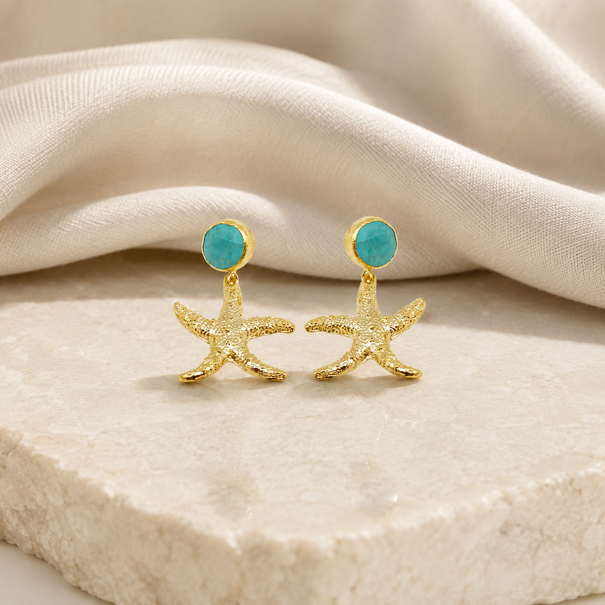 Gold starfish drop earrings with turquoise tops displayed on a clean background.