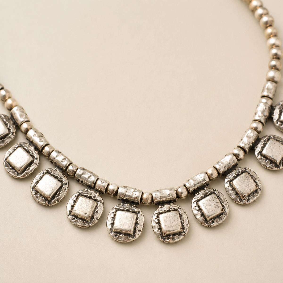 Close view of the necklace’s textured square drop details and bead strand.