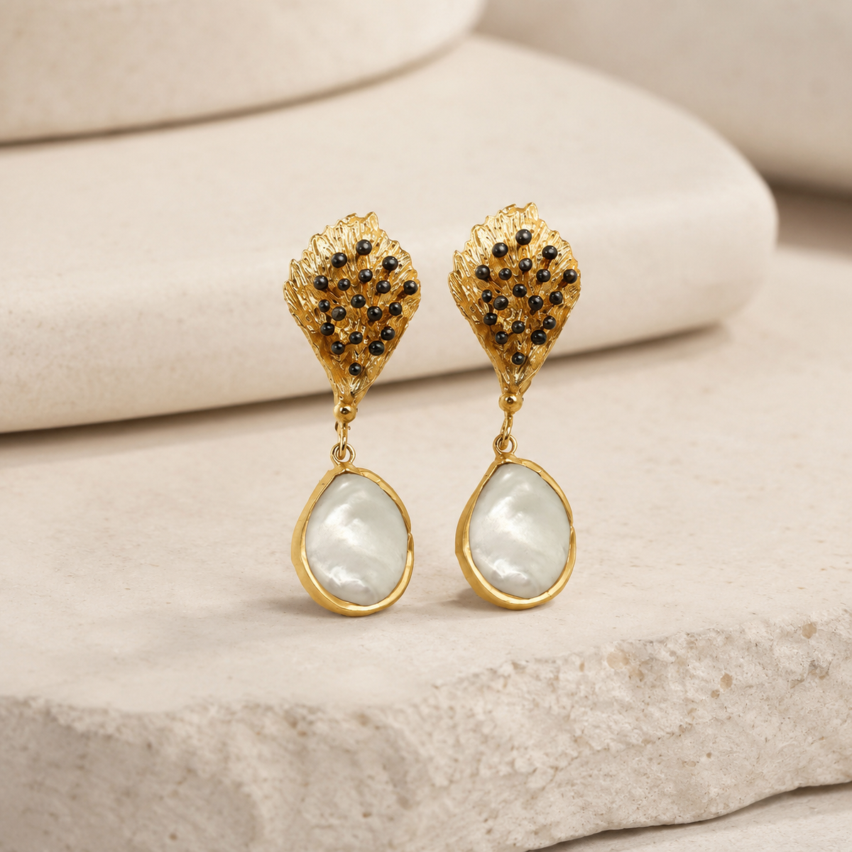 Angled view of gold-tone drop earrings with leaf-shaped tops and pearl-like teardrops.