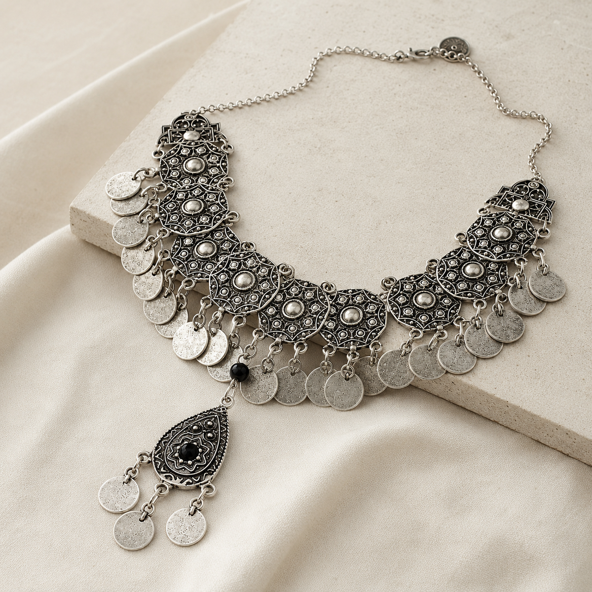 Angled view of a silver-tone bib necklace with coin fringe and black stone accents.