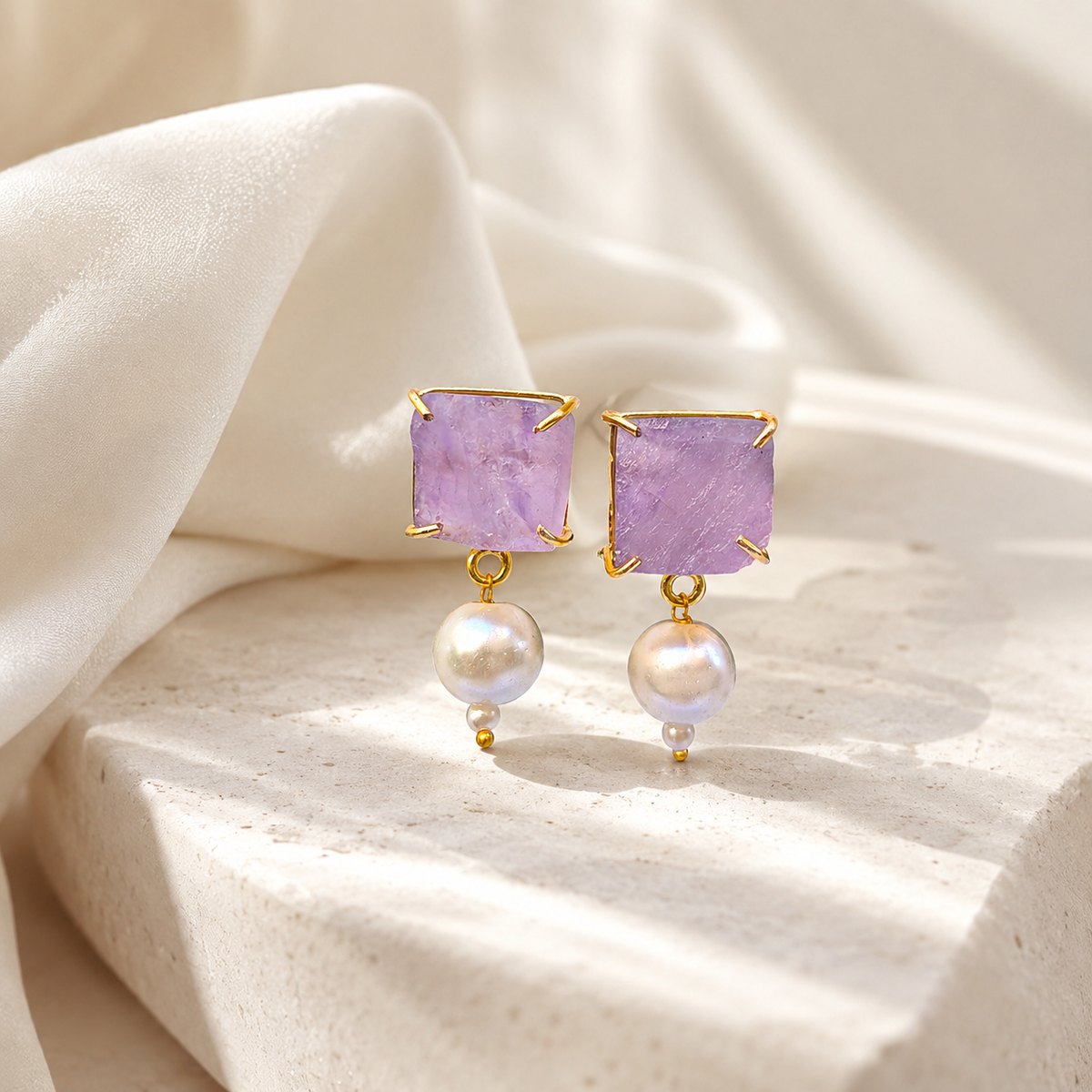 Gold-plated drop earrings with rough purple stones and pearl details on a white background.