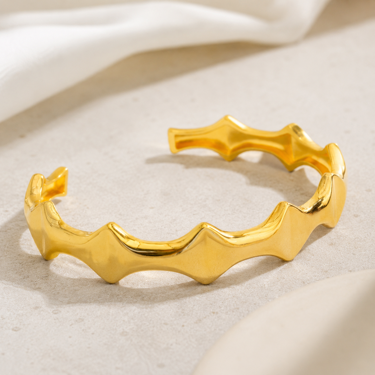 A polished gold-tone open cuff bracelet with a sculptural wave shape.