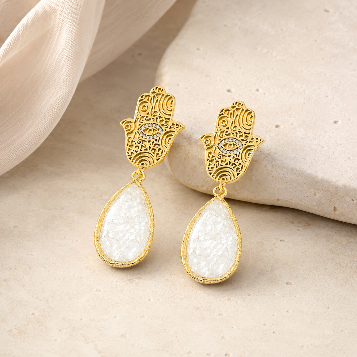 Gold hamsa hand earrings with white teardrop stones shown front view.
